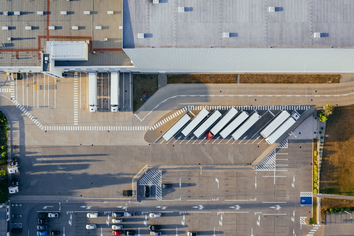 Aerial view of a logistics center with rows of trucks at warehouse loading docks, illustrating the handoff point between a freight forwarder and a 3PL.