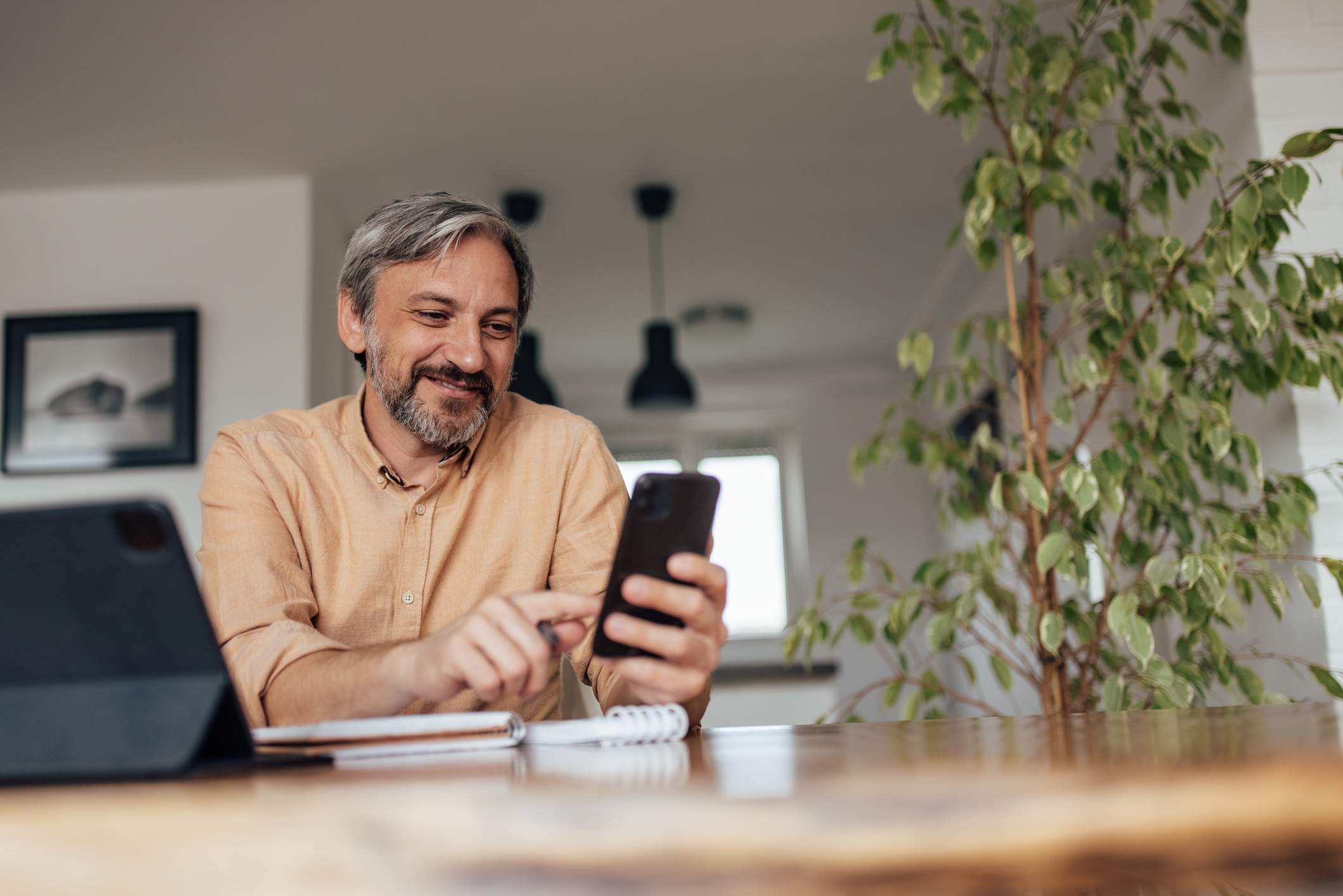 A man smiling while using his smartphone at a desk.