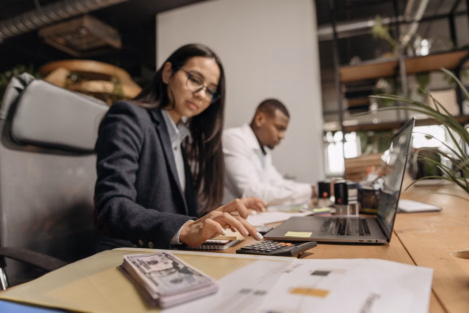 Two business professionals collaborating with a laptop and calculator