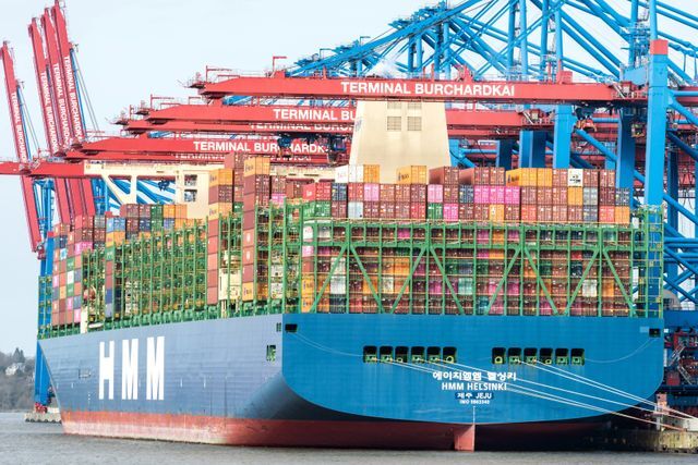 A large container ship moored at Hamburg's Burchardkai terminal during the day.